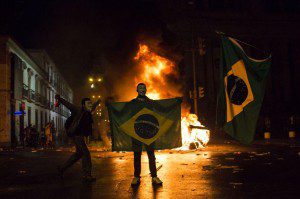 A demonstrator holds a Brazilian flag in front of a burning barricade during a protest in Rio de Janeiro in Rio de Janeiro, Brazil, Monday, June 17, 2013. Protesters massed in at least seven Brazilian cities Monday for another round of demonstrations voicing disgruntlement about life in the country, raising questions about security during big events like the current Confederations Cup and a papal visit next month. (AP Photo/Felipe Dana)