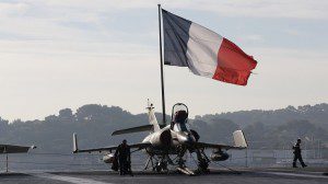 Flight deck crew work around a Super Etendard fighter jet as a French flag flies aboard the French nuclear-powered aircraft carrier Charles de Gaulle before its departure from the naval base of Toulon