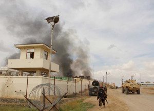 An Afghan security walks as smoke billows from a building after a Taliban attack in Gereshk district of Helmand province, Afghanistan